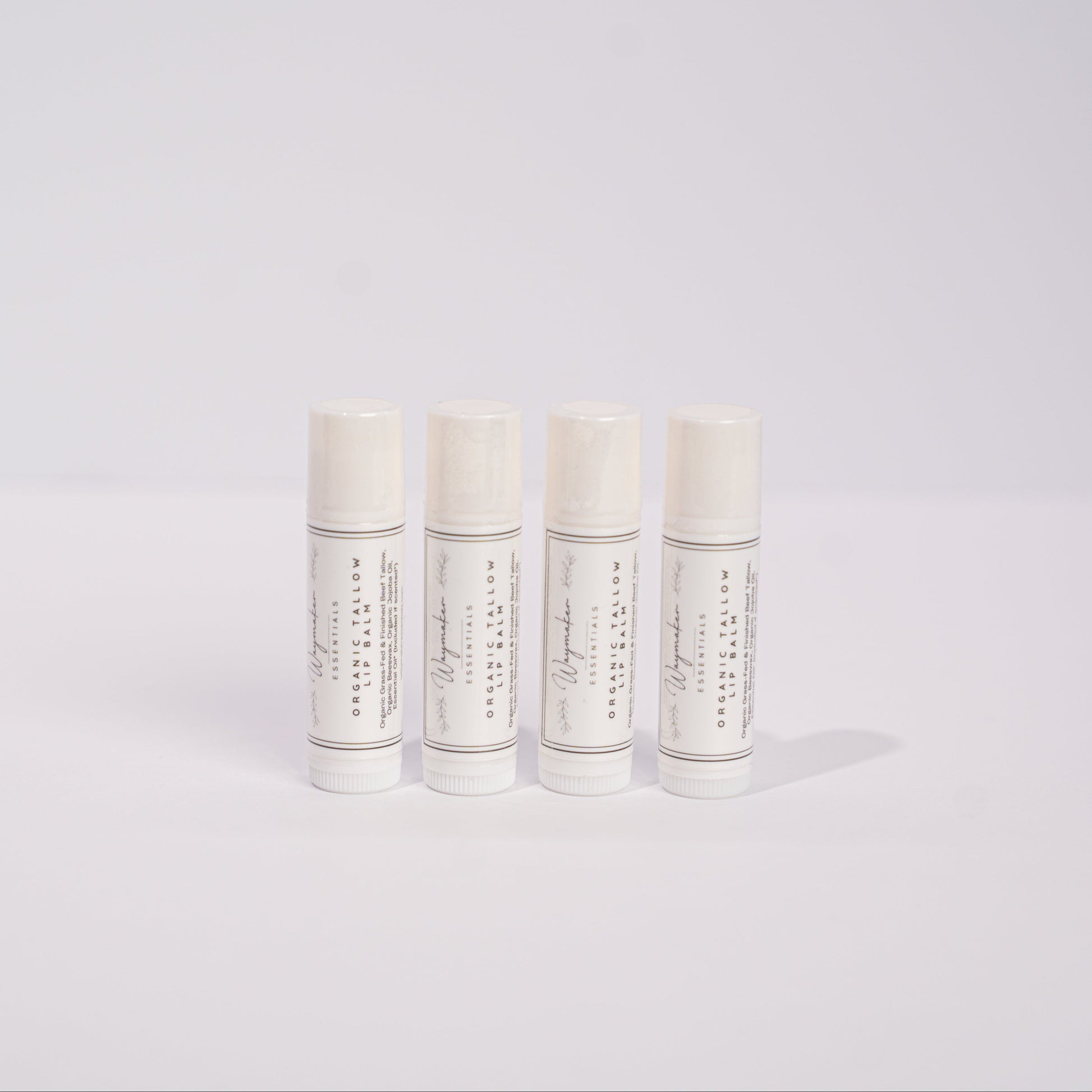 Four white rollerball bottles with black text on a light gray background - organic tallow lip balm