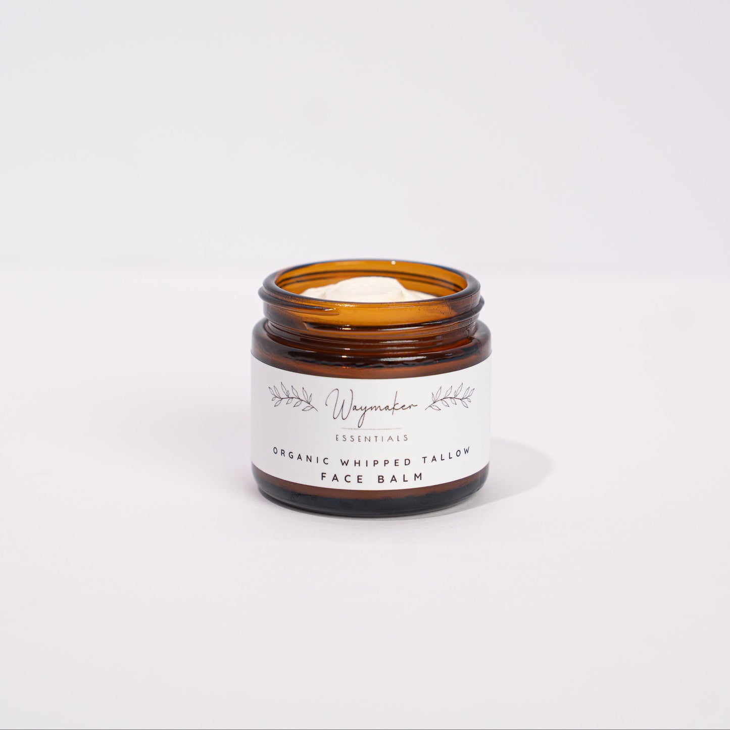 Small amber glass jar with a white label on a light gray background organic tallow face balm