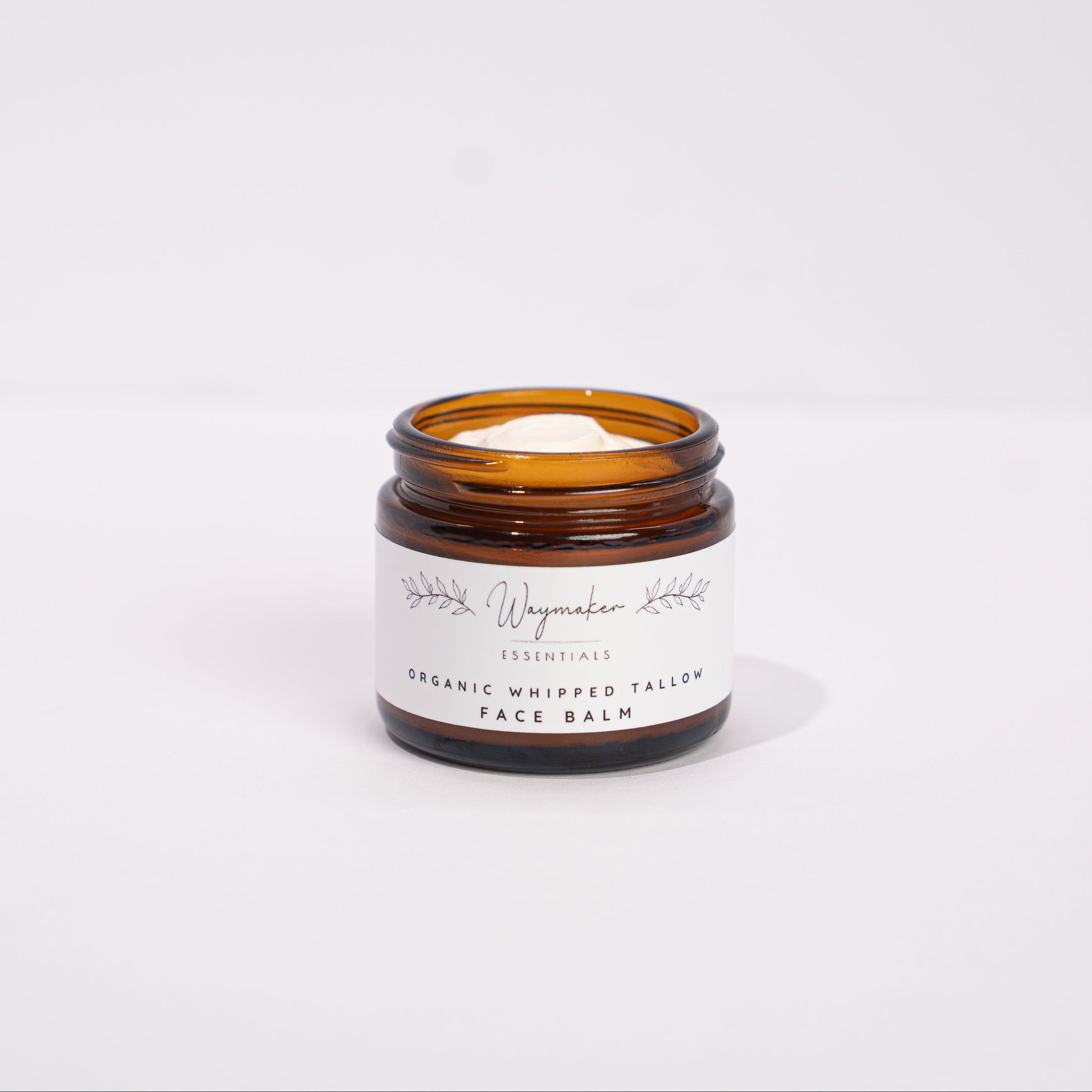 Small amber glass jar with a white label on a light gray background organic tallow face balm